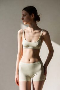 Zierliche KI-Schönheit in cremefarbenem Spitzen-BH und High-Waist-Höschen posiert elegant vor hellem Hintergrund mit sinnlichem Blick